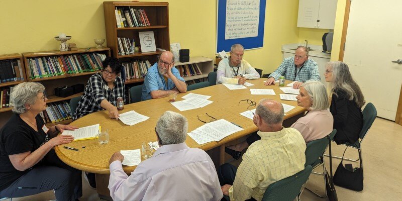 group of people around sit in conversation around a long table