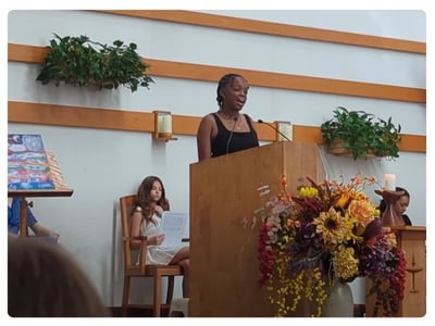 Gia Anderson stands in the pulpit at UU Fellowship of Huntington, her painting, 