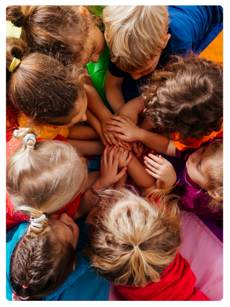 group of preschoolers lay on floor in tight circle with stacked hands