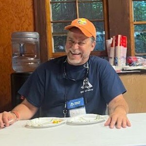 Matt is laughing during a camp game while wearing an orange camp cap